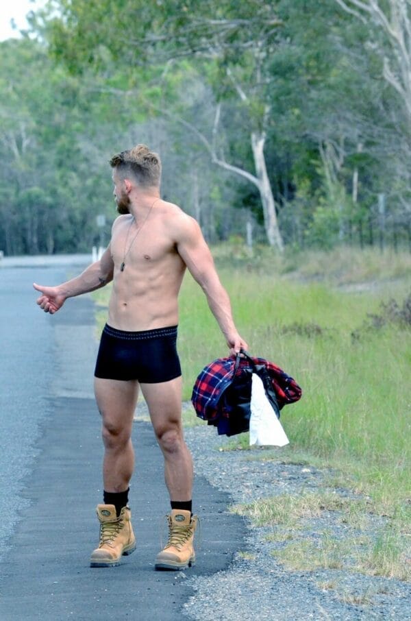 This is a photograph of a male model hitchhiking while only wearing a pair of black Bamboo Men's Trunks, available from Bamboo Creations Victoria